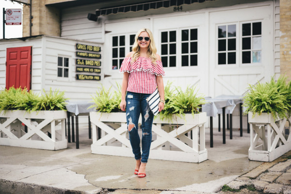 red and white gingham off the shoulder top with pom poms, ripped jeans, red ankle strap heels, striped clutch