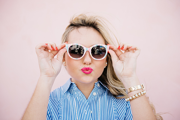 Bows & Sequins wearing striped sunglasses and bright pink lipstick.