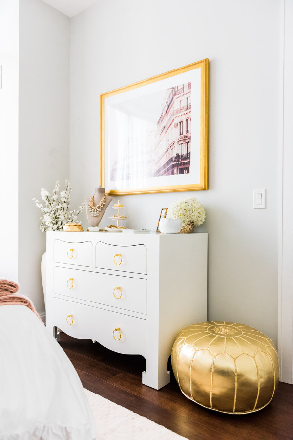 Blogger Jessica Sturdy of Bows & Sequins shares her Chicago Parisian-chic bedroom design. Bungalow 5 White Lacquer Jacqui Dresser with brass drawer pulls, Parisian facade print in an antique gold frame from Simply Framed, gold Moroccan leather pouf.