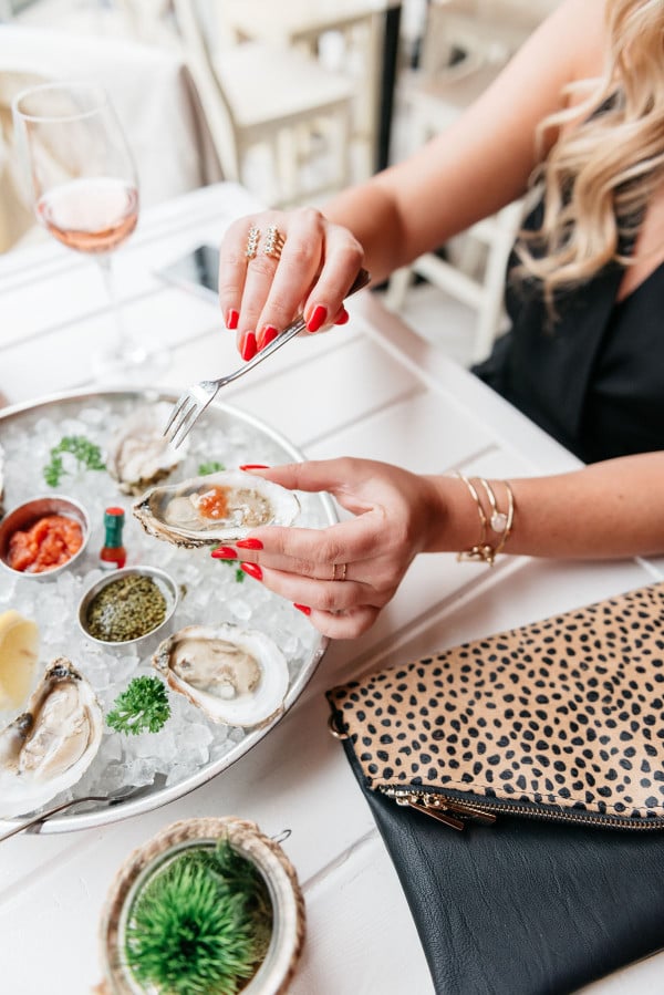 girl eating oysters, glass of rosé, leopard clutch