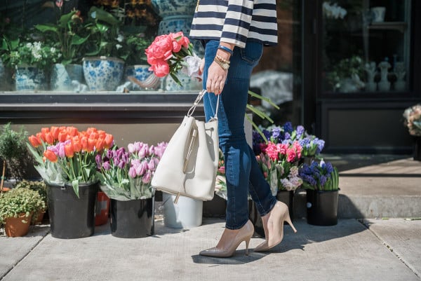 Bows & Sequins wearing a Tommy Hilfiger striped shirt, J Brand jeans, Kate Spade pumps, and a white bucket bag with a bouquet of pink peonies in Old Town Chicago. 