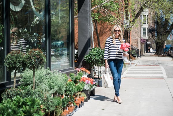 Bows & Sequins wearing a Tommy Hilfiger striped shirt, J Brand jeans, Kate Spade pumps, and a white bucket bag with a bouquet of pink peonies in Old Town Chicago. 