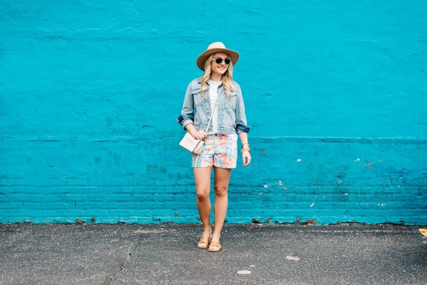 summer outfit colorful, jean jacket, white tee shirt, printed shorts, wide brim straw sun hat, leather slides sandals, pale pink crossbody bag