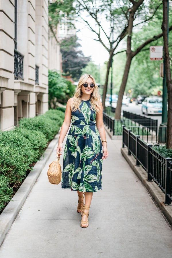 Blogger Jessica Sturdy (@bowsandsequins) wearing an Ann Taylor leaf print halter dress, Illesteva tortoise sunglasses, a J.McLaughlin wicker rattan handbag, and Ivanka Trump lace-up sandals in the Gold Coast in Chicago.