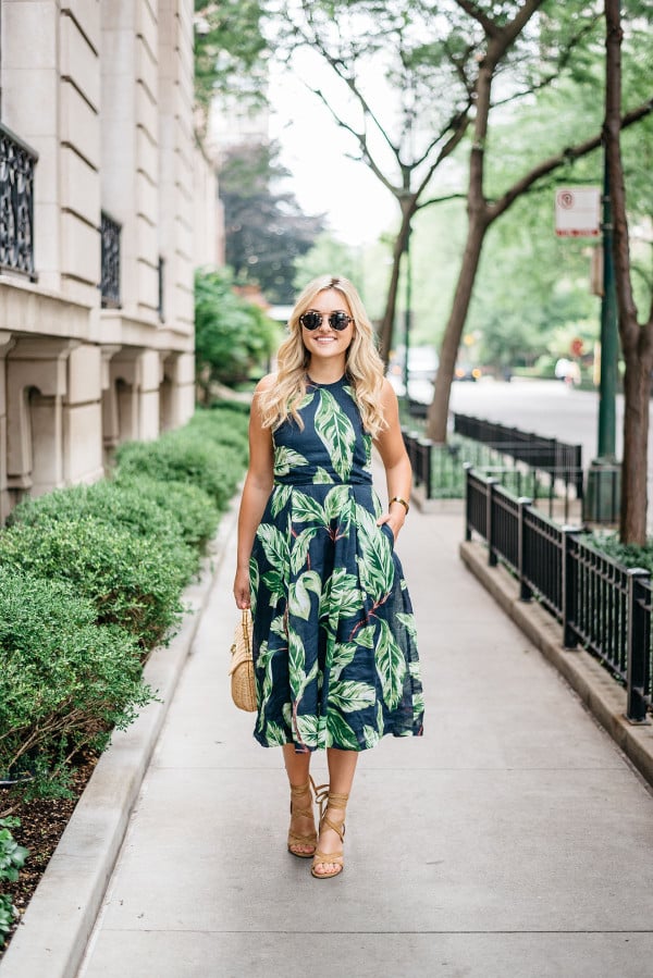 Blogger Jessica Sturdy (@bowsandsequins) wearing an Ann Taylor leaf print halter dress, Illesteva tortoise sunglasses, a J.McLaughlin wicker rattan handbag, and Ivanka Trump lace-up sandals in the Gold Coast in Chicago.