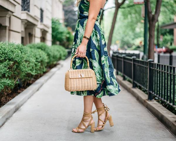 Blogger Jessica Sturdy (@bowsandsequins) wearing an Ann Taylor leaf print halter dress, Illesteva tortoise sunglasses, a J.McLaughlin wicker rattan handbag, and Ivanka Trump lace-up sandals in the Gold Coast in Chicago.