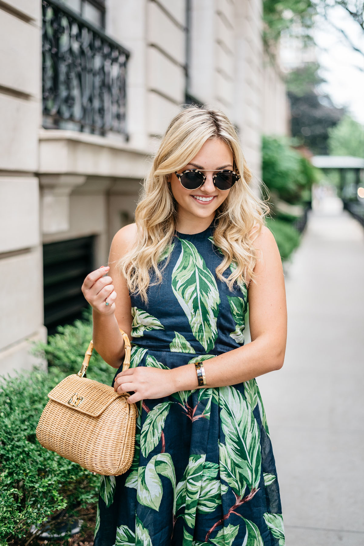 Blogger Jessica Sturdy (@bowsandsequins) wearing an Ann Taylor leaf print halter dress, Illesteva tortoise sunglasses, a J.McLaughlin wicker rattan handbag, and Ivanka Trump lace-up sandals in the Gold Coast in Chicago.