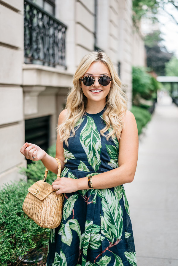 Blogger Jessica Sturdy (@bowsandsequins) wearing an Ann Taylor leaf print halter dress, Illesteva tortoise sunglasses, a J.McLaughlin wicker rattan handbag, and Ivanka Trump lace-up sandals in the Gold Coast in Chicago.