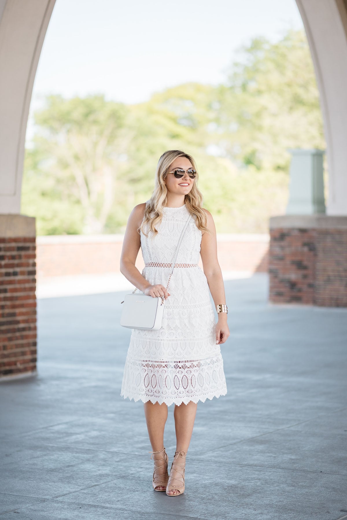Bows & Sequins wearing a white lace dress, white crossbody bag, and tan lace-up heels in Chicago.