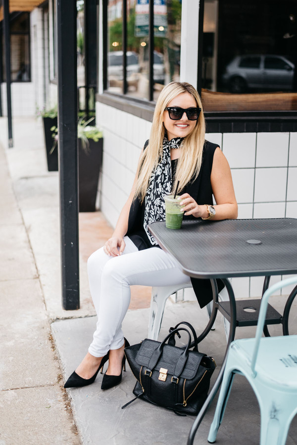 Bows & Sequins styles a casual summertime work outfit: white denim jeans, a silky blank tank top, a long black vest, a scarf tied at the neck, black pointed toe pumps, and a black tote!
