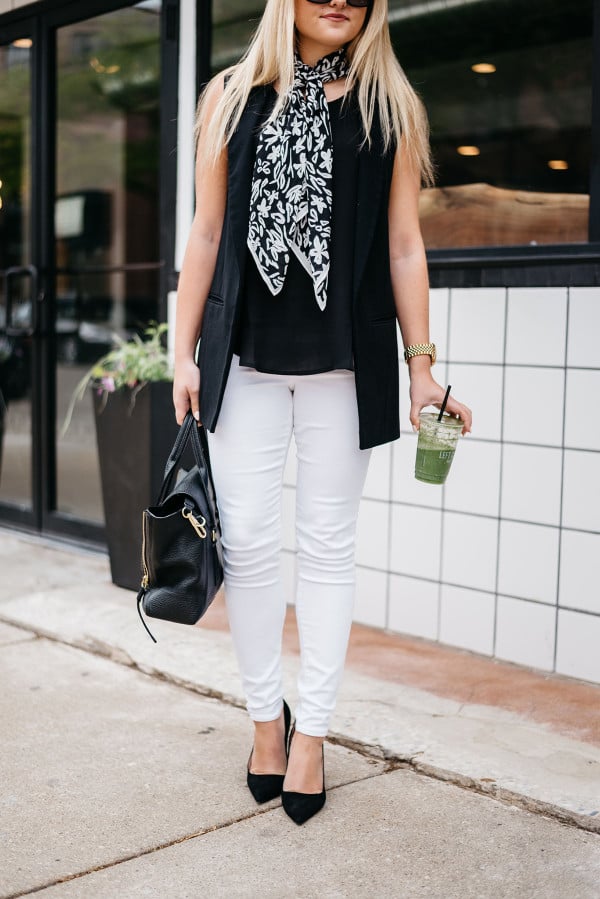 Bows & Sequins styles a casual summertime work outfit: white denim jeans, a silky blank tank top, a long black vest, a scarf tied at the neck, black pointed toe pumps, and a black tote!