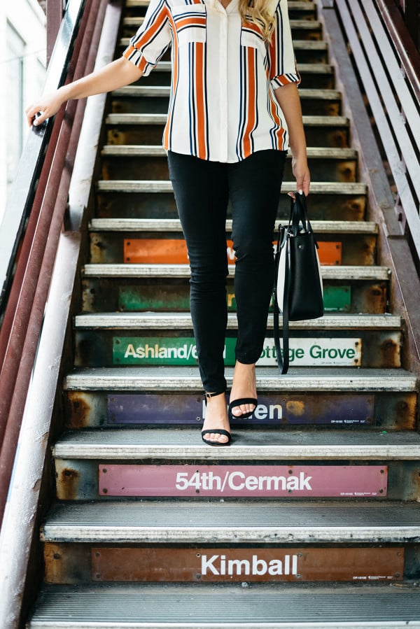 Chicago Blogger Jessica Sturdy of Bows & Sequins styling a striped button-front shirt, black skinny jeans, ankle-strap heels, and a color-blocked black and white tote for a work-appropriate outfit in front of the Chicago El Train steps in the Loop downtown.
