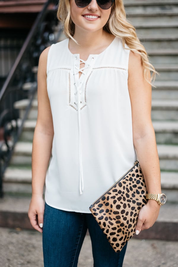 Bows & Sequins wearing a white sleeveless blouse, J Brand jeans, and a leopard clutch.