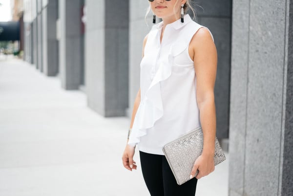 Bows & Sequins styling a white ruffled sleeveless collared shirt, black destroyed denim, tassel drop earrings, a metallic cut-out clutch, and black Ray-Ban aviator sunglasses.