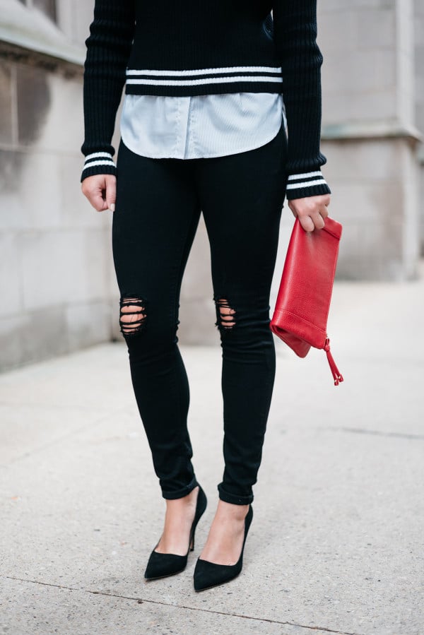 Fashion blogger Bows & Sequins wearing black ripped jeans and a red clutch purse.