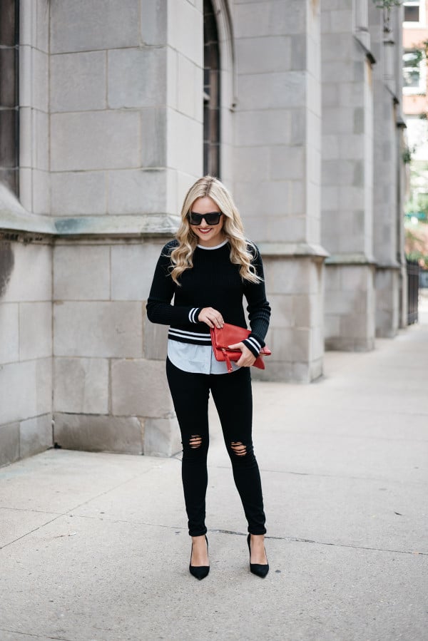 Fashion blogger Bows & Sequins styling a black and white sweater, black jeans with rips at the knees, black pumps, sunglasses, and a red purse.