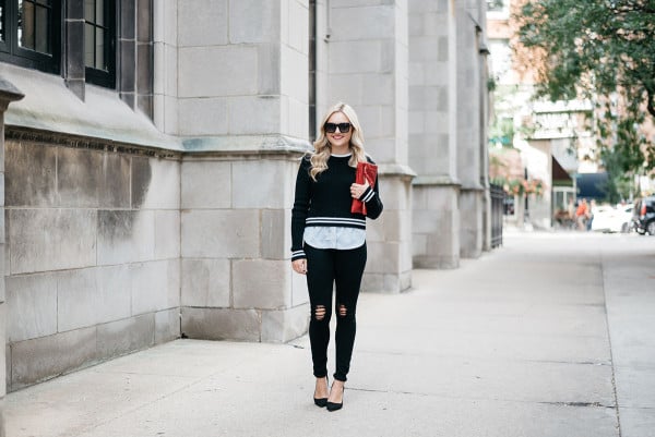 Fashion blogger Bows & Sequins wearing a black and white stripe Nordstrom sweater, black ripped jeans, black heels, and a red clutch purse.
