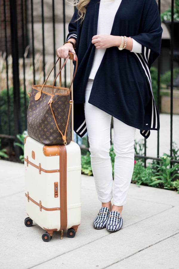 Bows & Sequins wearing a stylish and easy outfit for traveling: navy striped sweater, white corduroy pants, Gucci gingham loafers, Louis Vuitton Neverfull Tote, and Bric's Bellagio cream spinner suitcase. Comfortable, but chic!
