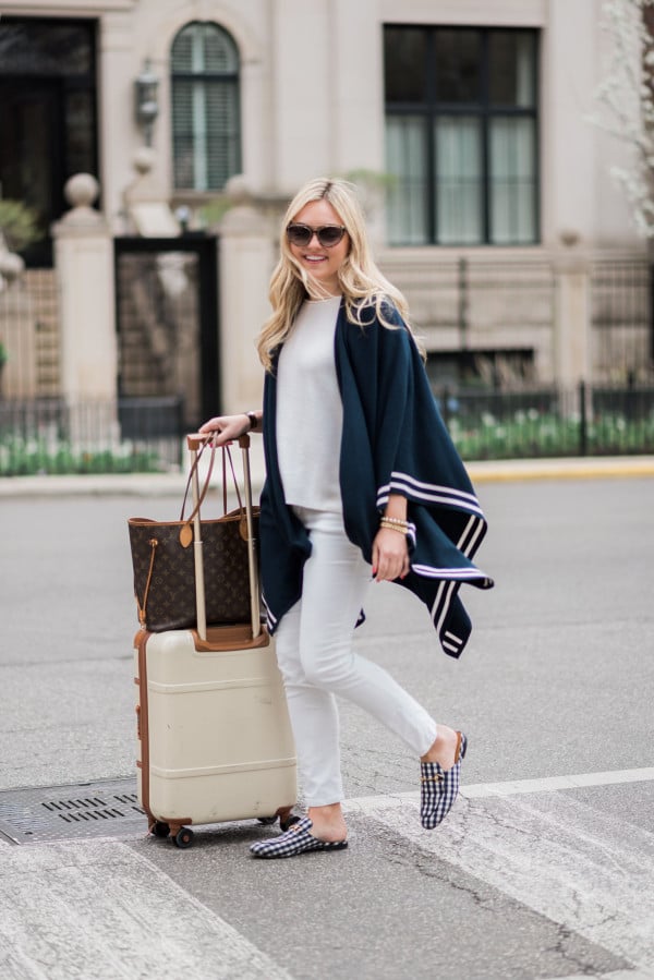 Bows & Sequins wearing a stylish and easy outfit for traveling: navy striped sweater, white corduroy pants, Gucci gingham loafers, Louis Vuitton Neverfull Tote, Bric's Bellagio cream spinner suitcase, and Tom Ford sunglasses. Comfortable, but chic!