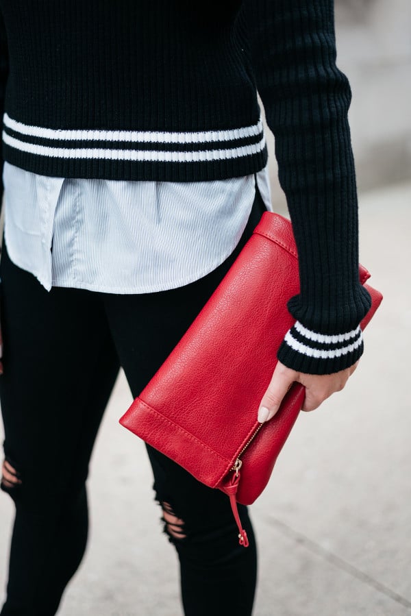 Fashion blogger Jessica Sturdy wearing a black and white sweater, black jeans, and a red clutch purse.