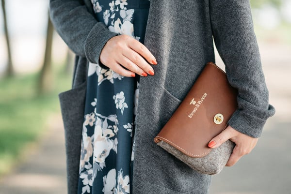 Jessica Sturdy of Bows & Sequins wearing a navy floral dress, grey sweater, and tan and grey wool clutch.