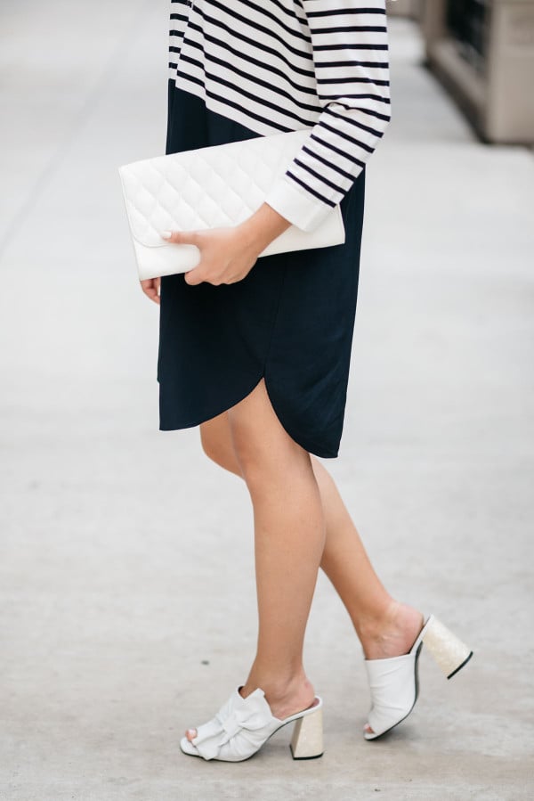 Fashion blogger Bows & Sequins styling a striped t-shirt dress, white bow shoes, and a white clutch purse.