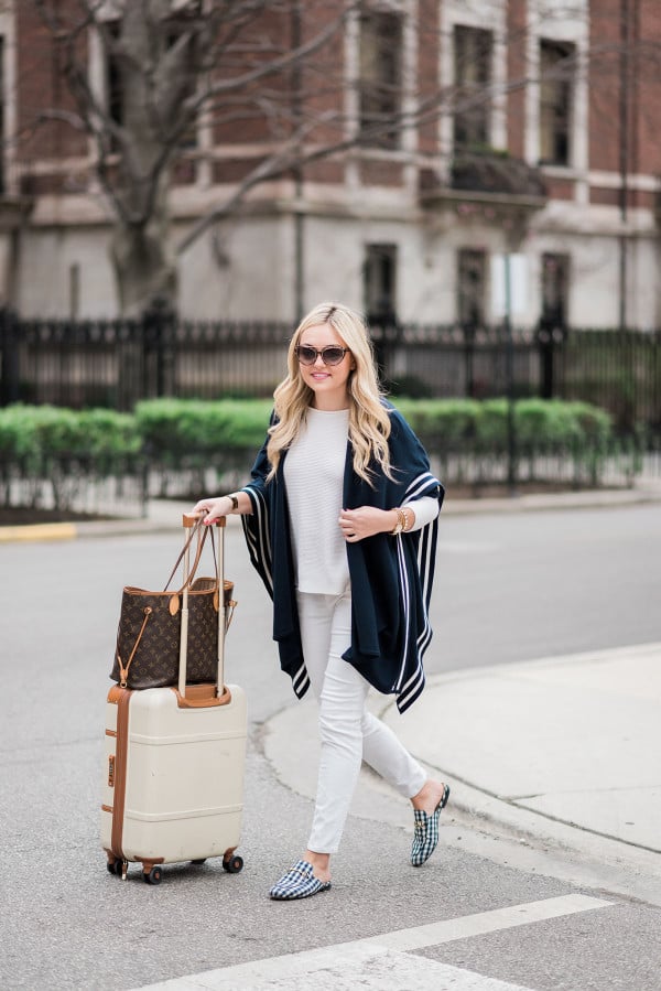 Bows & Sequins wearing a stylish and easy outfit for traveling: navy striped sweater, white corduroy pants, Gucci gingham loafers, Louis Vuitton Neverfull Tote, Bric's Bellagio cream spinner suitcase, and Tom Ford sunglasses. Comfortable, but chic!