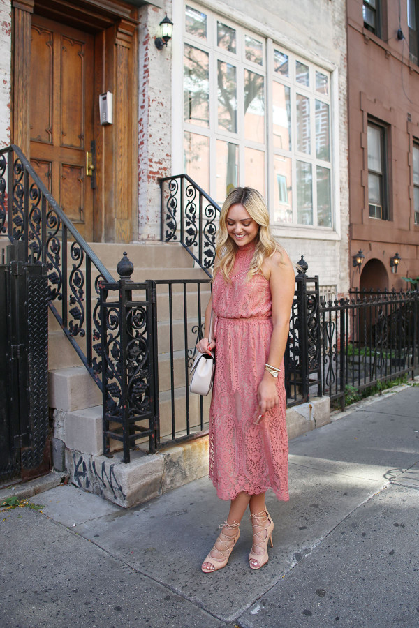 Fashion blogger Bows & Sequins wearing a pink lace midi dress during New York Fashion Week. Jessica styled the outfit with nude lace-up sandals, a Kate Spade crossbody bag, and blush pink square cat-eye sunglasses. Makeup was done by Mary Kay via GlamSquad!