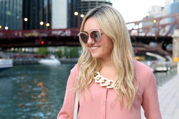 Bows & Sequins wearing blush pink sunglasses, a rosy button-front blouse, and a white link necklace.