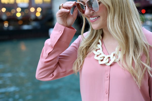 Bows & Sequins wearing blush pink sunglasses, a rosy button-front blouse, and a white link necklace.