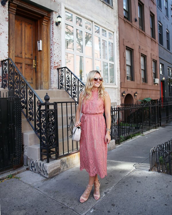 Fashion blogger Bows & Sequins wearing a pink lace midi dress during New York Fashion Week. Jessica styled the outfit with nude lace-up sandals, a Kate Spade crossbody bag, and blush pink square cat-eye sunglasses. Makeup was done by Mary Kay via GlamSquad!