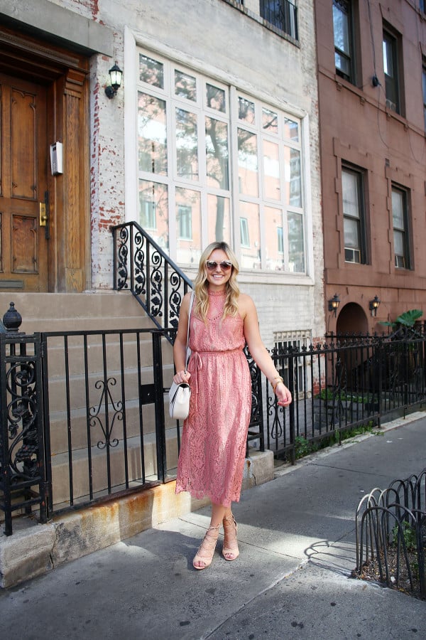 Fashion blogger Bows & Sequins wearing a pink lace midi dress during New York Fashion Week. Jessica styled the outfit with nude lace-up sandals, a Kate Spade crossbody bag, and blush pink square cat-eye sunglasses. Makeup was done by Mary Kay via GlamSquad!