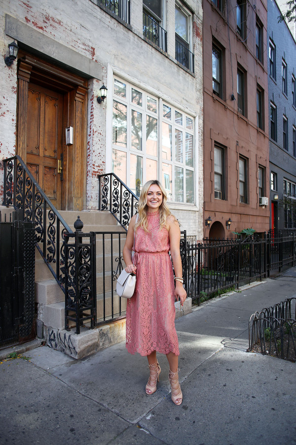 Fashion blogger Bows & Sequins wearing a pink lace midi dress during New York Fashion Week. Jessica styled the outfit with nude lace-up sandals, a Kate Spade crossbody bag, and blush pink square cat-eye sunglasses. Makeup was done by Mary Kay via GlamSquad!