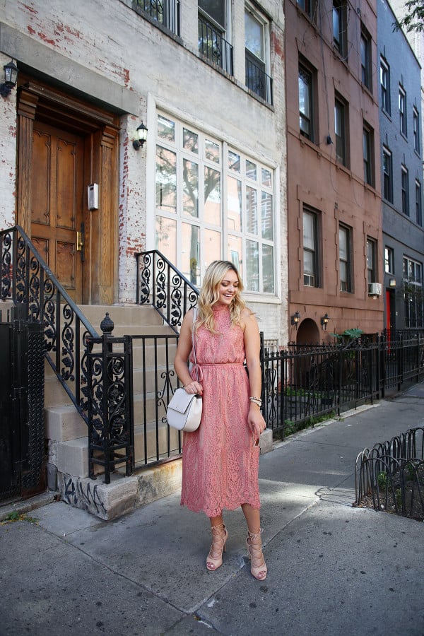 Fashion blogger Bows & Sequins wearing a pink lace midi dress during New York Fashion Week. Jessica styled the outfit with nude lace-up sandals, a Kate Spade crossbody bag, and blush pink square cat-eye sunglasses. Makeup was done by Mary Kay via GlamSquad!