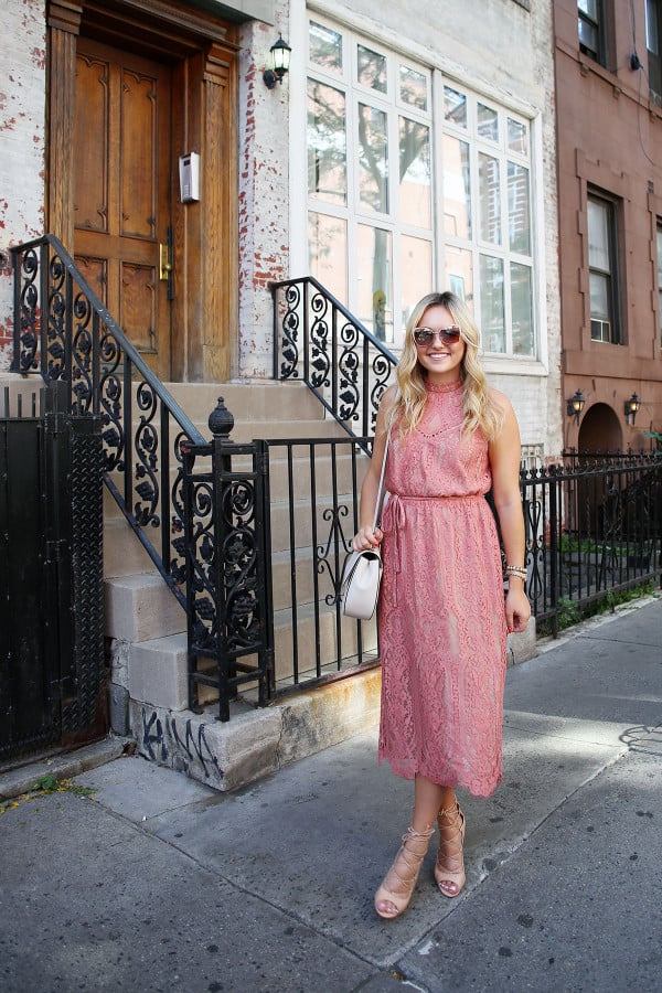Fashion blogger Bows & Sequins wearing a pink lace midi dress during New York Fashion Week. Jessica styled the outfit with nude lace-up sandals, a Kate Spade crossbody bag, and blush pink square cat-eye sunglasses. Makeup was done by Mary Kay via GlamSquad!