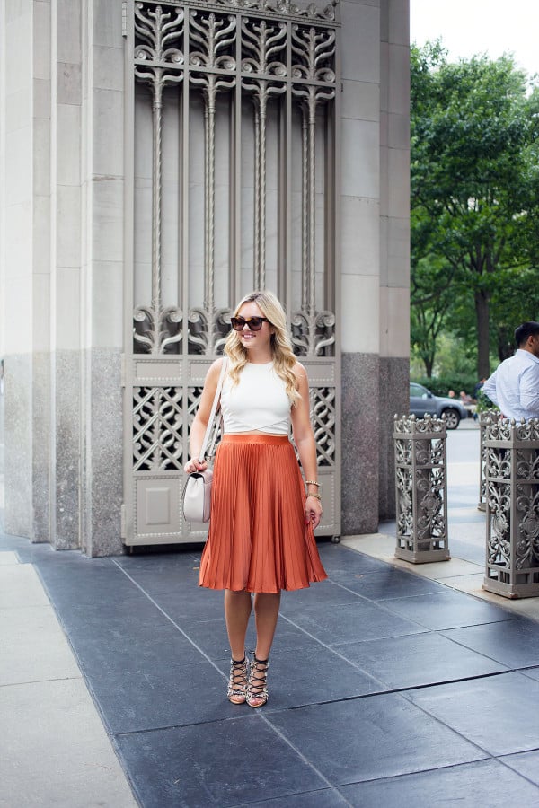 Pleated skirts are one of fall's hottest trends! Blogger Bows & Sequins styles hers with a crop-top tank, lace-up leopard heels, oversized sunglasses, and a round crossbody bag.