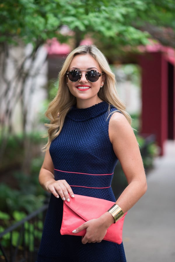 Style blogger Jessica Sturdy of Bows & Sequins wearing a navy blue dress with coral accents, coral purse, and sunglasses in Chicago.