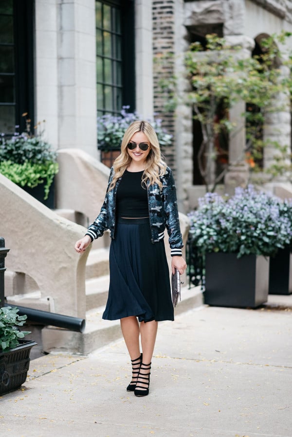 Bows & Sequins styling a sequin bomber jacket, crop top, pleated midi skirt, and military-inspired pumps for fall.