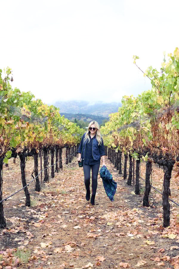 Bows & Sequins wearing a plaid shirt, quilted vest, grey jeans, black booties, and a blanket scarf in Napa, California.