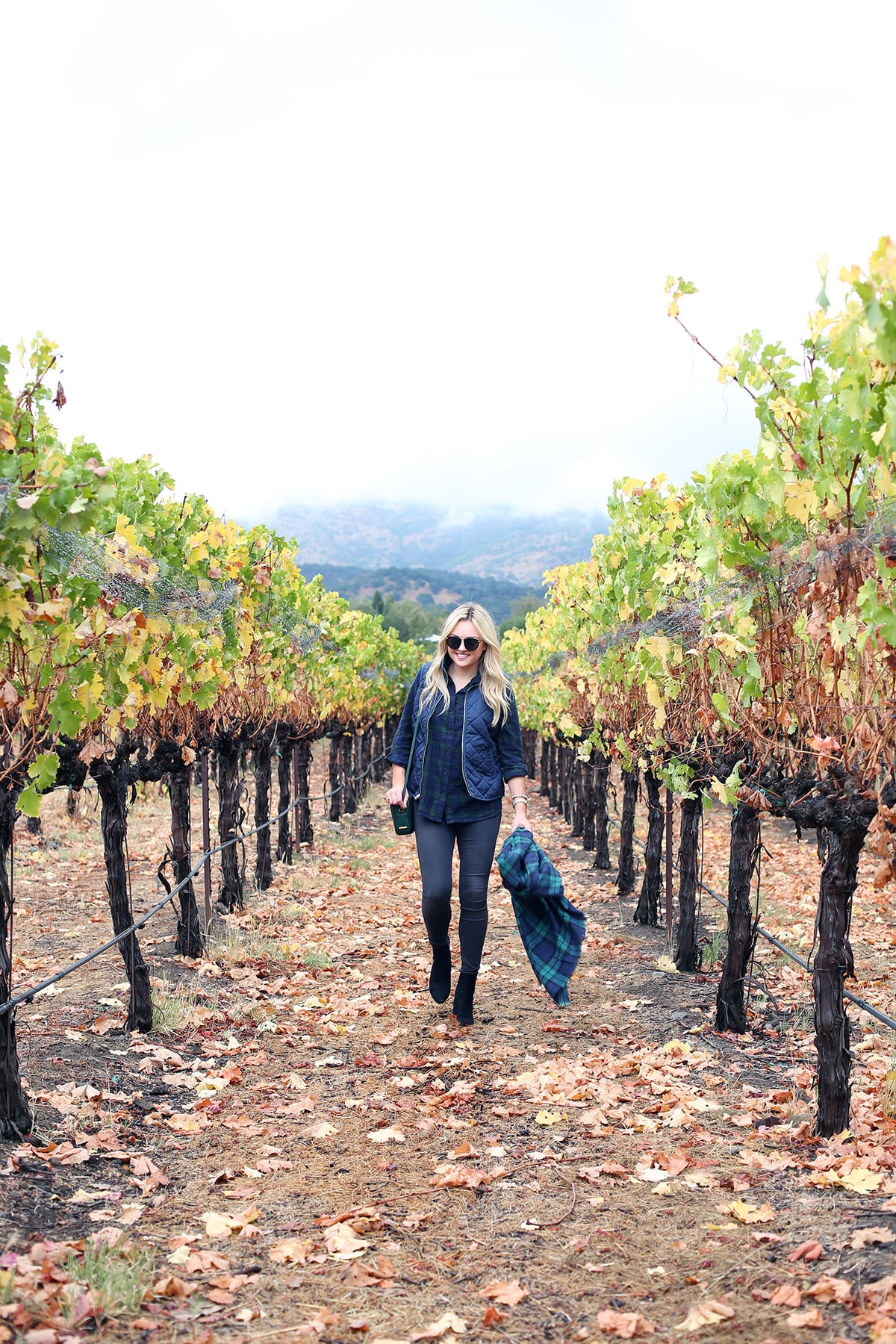 Bows & Sequins wearing a plaid shirt, quilted vest, grey jeans, black booties, and a blanket scarf in Napa, California.