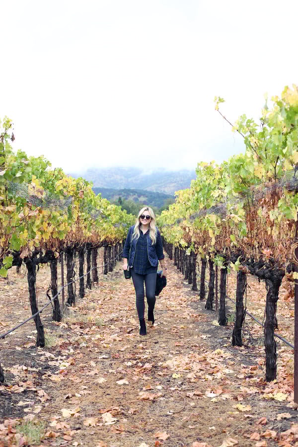 Bows & Sequins wearing a plaid shirt, quilted vest, grey jeans, black booties, and a blanket scarf in Napa, California.