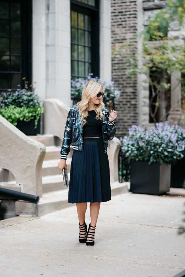 Bows & Sequins styling a sequin bomber jacket, crop top, pleated midi skirt, and military-inspired pumps for fall.