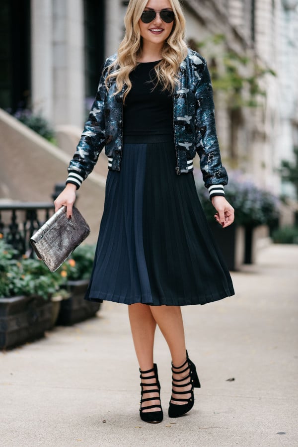 Bows & Sequins styling a sequin bomber jacket, crop top, pleated midi skirt, and military-inspired pumps for fall.