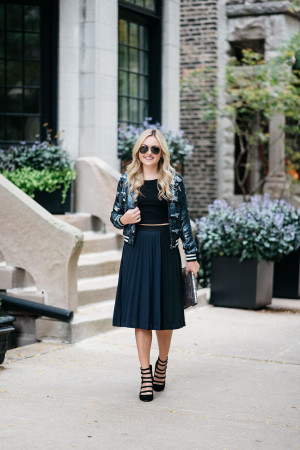 Bows & Sequins styling a sequin bomber jacket, crop top, pleated midi skirt, and military-inspired pumps for fall.