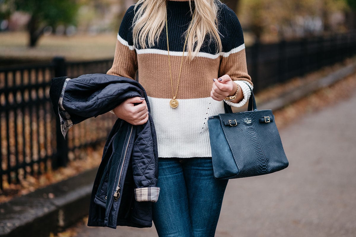 Bows & Sequins wearing a casual outfit for Thanksgiving: a striped, mockneck sweater, dark denim, a simple pendant necklace, a navy blue Kate Spade bag, and a quilted Barbour jacket.