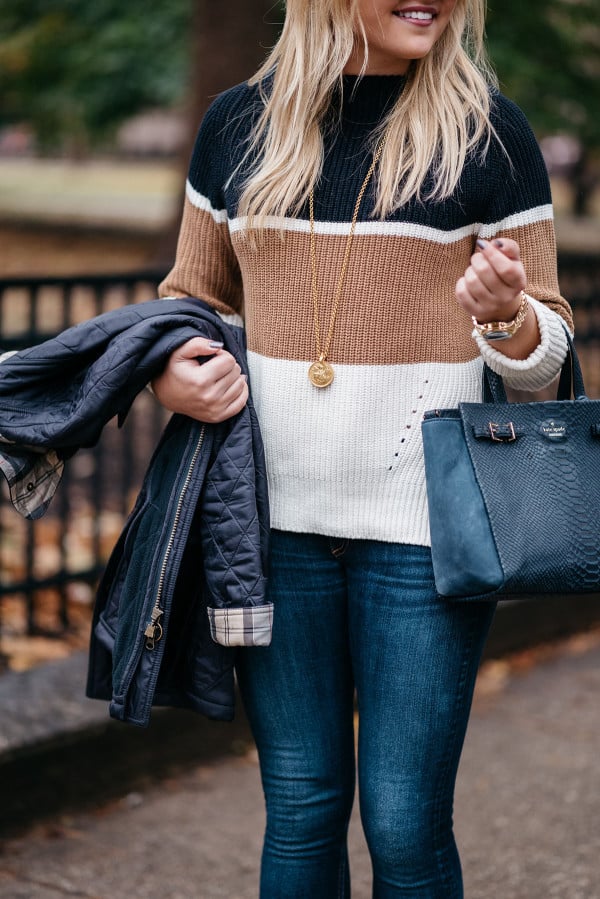 Bows & Sequins wearing a casual outfit for Thanksgiving: a striped, mockneck sweater, dark denim, a simple pendant necklace, a navy blue Kate Spade bag, and a quilted Barbour jacket.