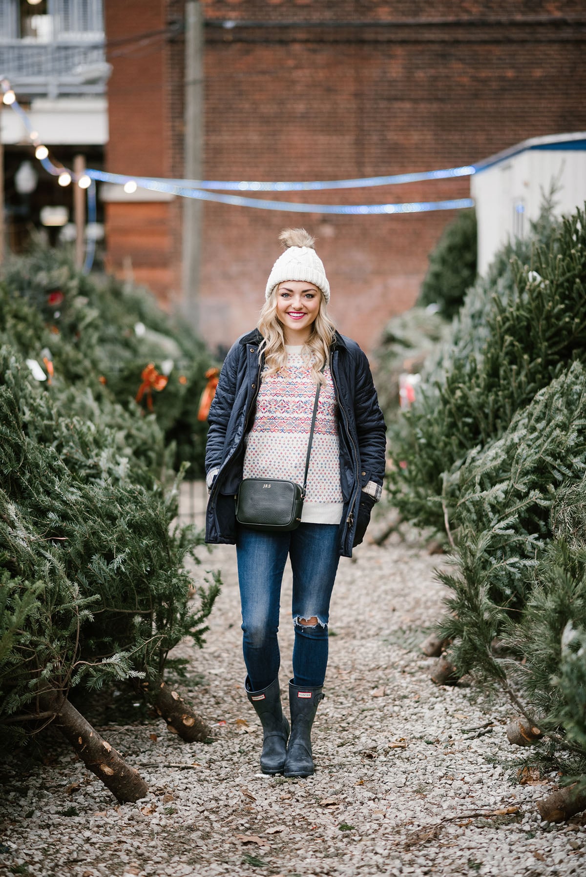 Bows & Sequins wearing a Barbour coat, a colorful Christmas sweater, Hunter boots, and a beanie to pick out a tree in the city.