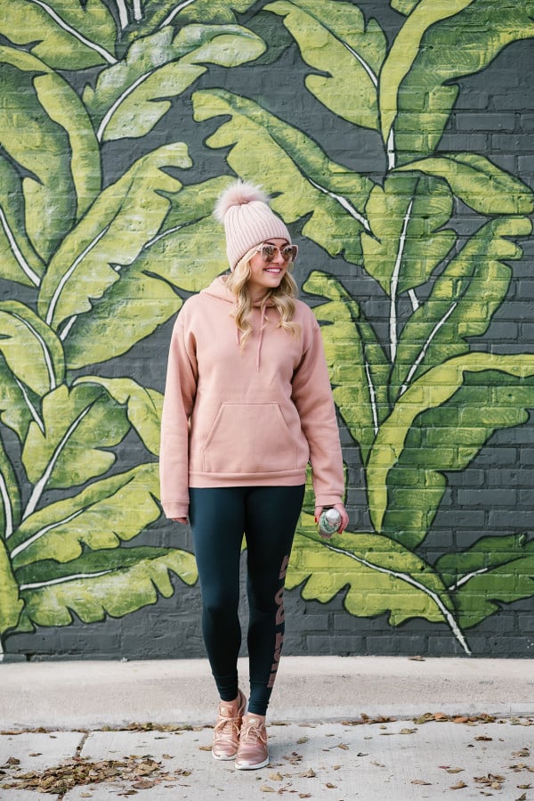 Chicago-based blogger, Jessica Sturdy, wearing a pink and navy workout outfit in front of the palm leaf wall at Eden in the West Loop.