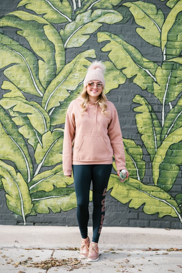 Bows & Sequins wearing cold weather workout wear in front of the palm leaf mural at Eden Chicago.