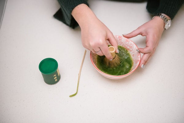 Bows & Sequins mixing matcha tea powder with a bamboo whisk.